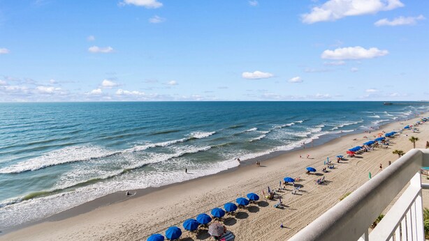 A beach with waves, umbrellas, and people. - Garden City Beach Oceanfront Condo 609 | Rising Tides Properties Rental (Murrells Inlet)