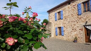 Um edifício de pedra com portaria azul, um pátio de cascalho e rosas em flor.