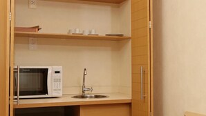 A compact kitchen with a built-in microwave, a sink, and wooden cabinets. - Riema Paulista Classic Flat Service (São Paulo)