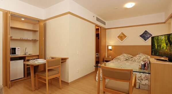A compact hotel room with a kitchenette, a bed with a TV, and a small desk area.