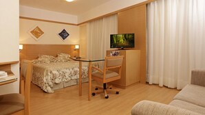 A hotel room with a bed, a desk with a chair, a television, and a couch. - Riema Paulista Classic Flat Service (São Paulo)