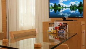 A hotel room with a glass dining table, wooden chairs, a television on a wooden cabinet, and a view of a lake through the window. - Riema Paulista Classic Flat Service (São Paulo)