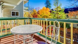 A wooden deck with a round metal table and chairs, a yellow railing, and a view of colorful autumn trees and a building in the background. - Originally built in Chautauqua Institution in 1890, the original St. Elmo Hotel building was torn down and rebuilt as a residential condominium.  It now offers the convenience of an elevator; (Chautauqua)