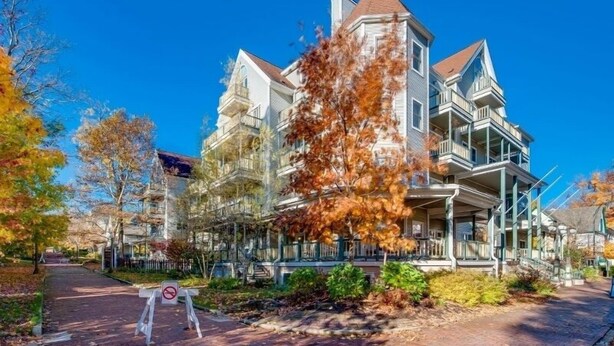A large, multi-story building with a prominent tower and multiple balconies, surrounded by trees with autumn foliage. - Originally built in Chautauqua Institution in 1890, the original St. Elmo Hotel building was torn down and rebuilt as a residential condominium.  It now offers the convenience of an elevator; (Chautauqua)