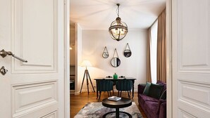 Une pièce comprenant une table basse ronde, un canapé violet, une table à manger avec des chaises et un lustre.