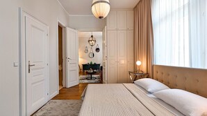 Une chambre à coucher comprenant un lit, une table de chevet, un luminaire suspendu, une armoire et donnant sur un couloir.