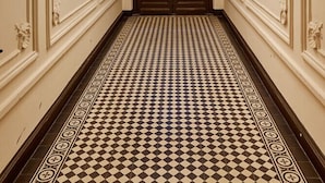 Un couloir doté d’un sol à carreaux, de moulures murales décoratives et d’un lustre.