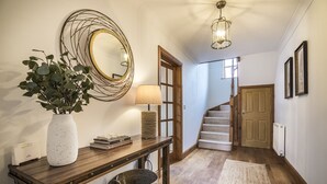 A hallway with a wooden console table, a potted plant, a lamp, and a mirror. There is a staircase leading to another room. - French Fields - 4 Bedroom - St Florence (Tenby)
