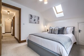 A bedroom with a large bed, a skylight, a hallway, and a door. - French Fields - 4 Bedroom - St Florence (Tenby)