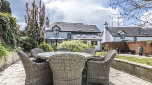 A patio with wicker furniture and a view of a house with a sloped roof and a chimney. - French Fields - 4 Bedroom - St Florence (Tenby)