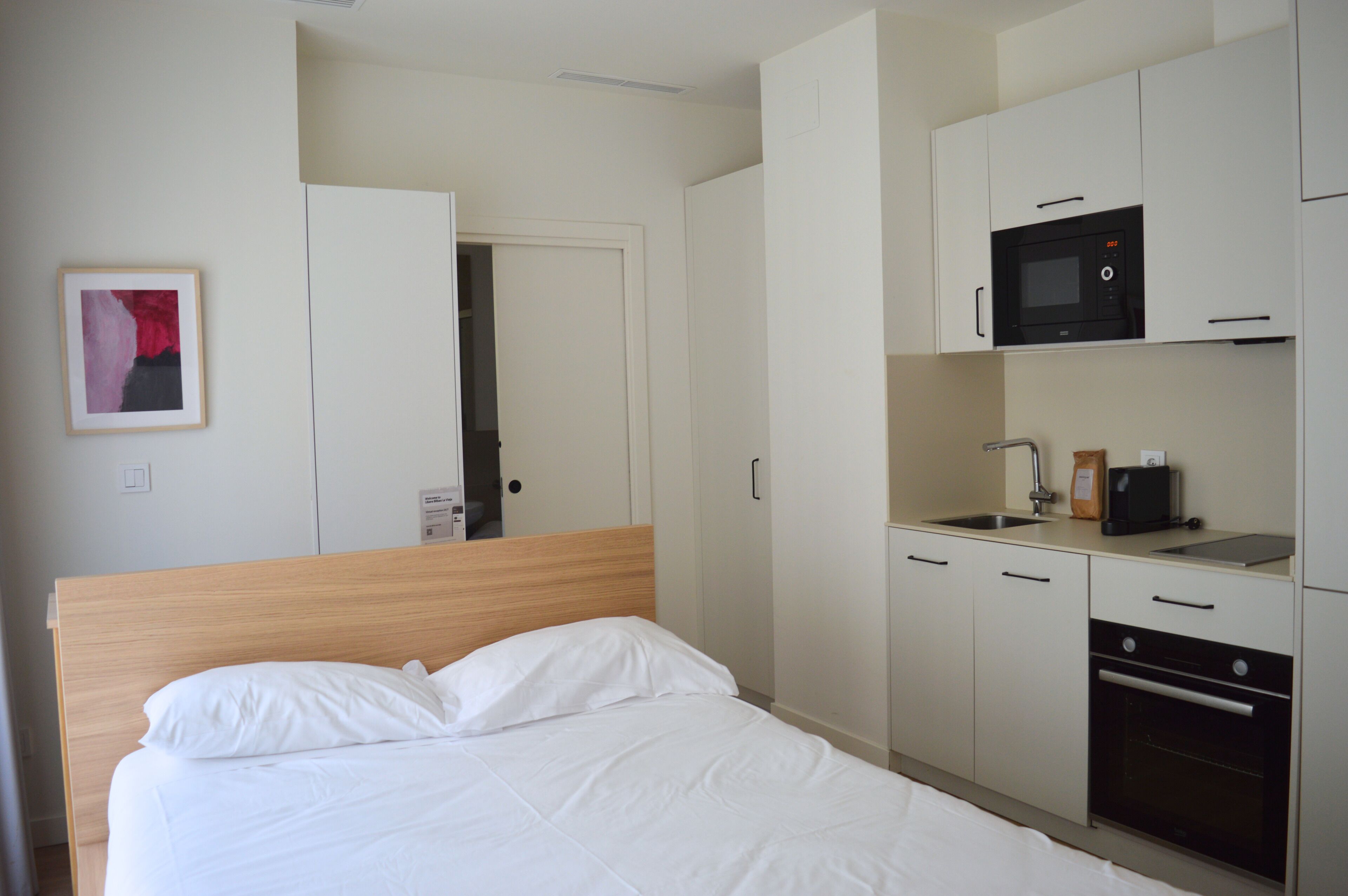 A hotel room with a bed, a kitchenette with a microwave, a coffee maker, and a sink.