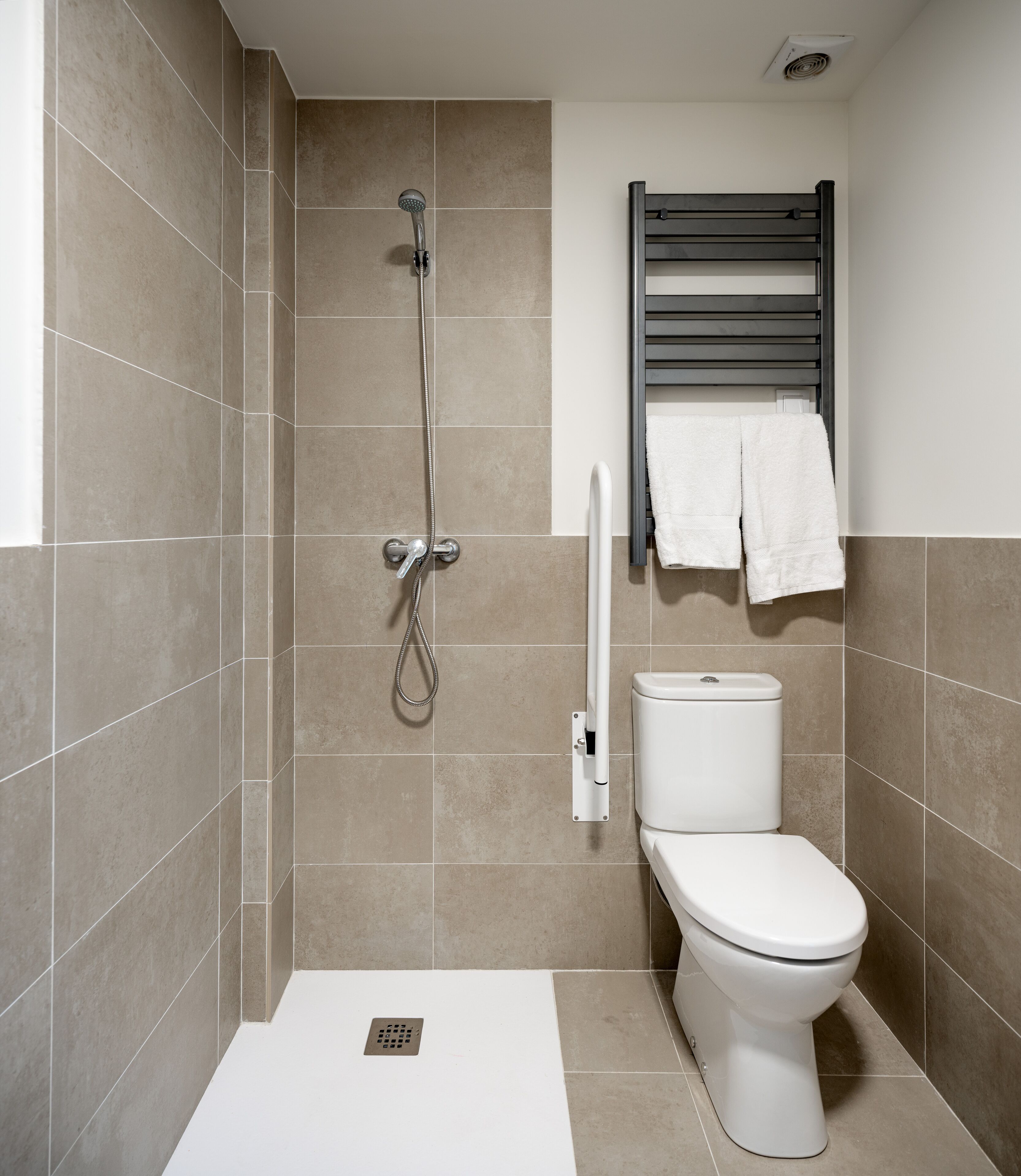 Een moderne badkamer met douche, toilet en handdoekhouder.