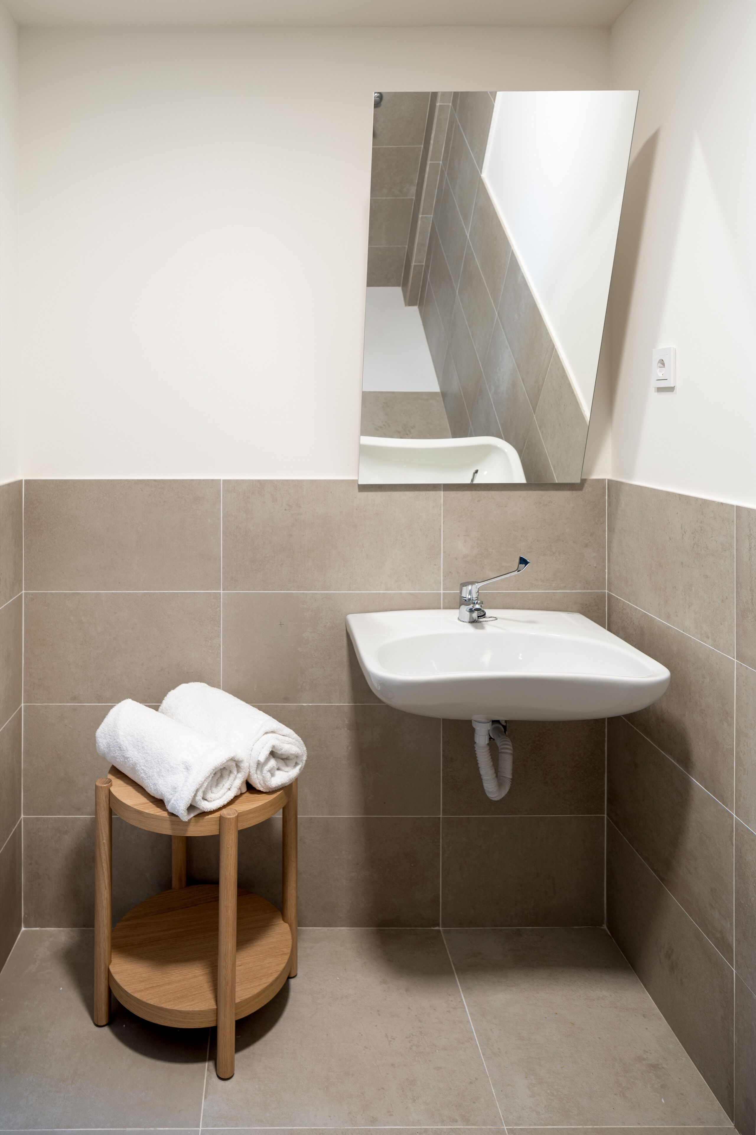 Un baño con lavamanos, espejo y un taburete de madera redondo con toallas.