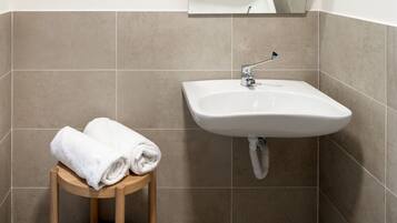 Un baño con lavamanos, espejo y un taburete de madera redondo con toallas.