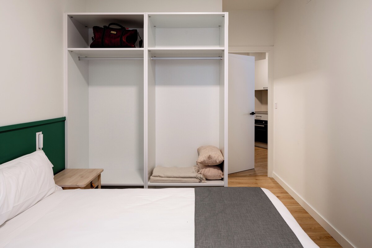 Une chambre à coucher comprenant un lit, une armoire, une table de chevet et un petit coin salon avec des coussins.