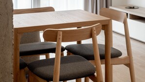 Een moderne eetruimte met een houten tafel en stoelen, een televisie aan de muur, en een uitzicht door een raam met transparante gordijnen.
