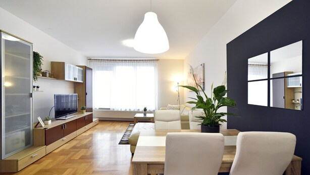 Ein modernes Wohnzimmer mit Holzboden, einem Esstisch mit Stühlen, einer Couch, einem Fernseher und einem großen Fenster mit Vorhängen.