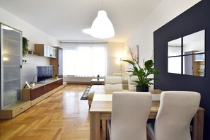 A modern living room with a wooden floor, a dining table with chairs, a sofa, a TV, and a large window with curtains. - Apartment Stadium (Zagreb)