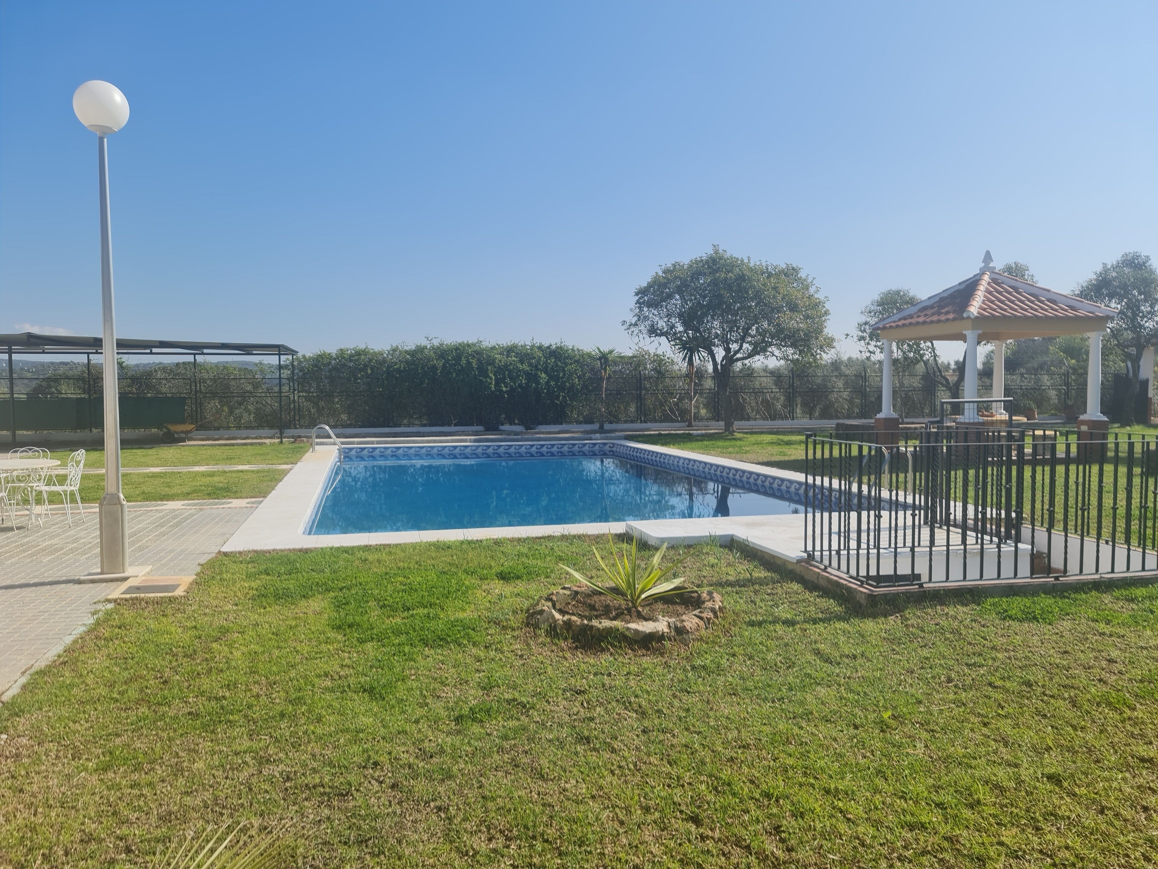 Ein Schwimmbad mit einer Pergola und einem Pavillon in einem angelegten Garten.
