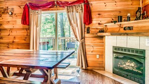Interno di una baita in legno con camino, tavolo da pranzo e tende.