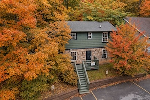 A two-story house with a stone facade, a green roof, and a staircase leading to the entrance.
