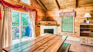 Interno di una baita in legno con un tavolo da pranzo, angolo cottura e vista attraverso una porta vetrata.