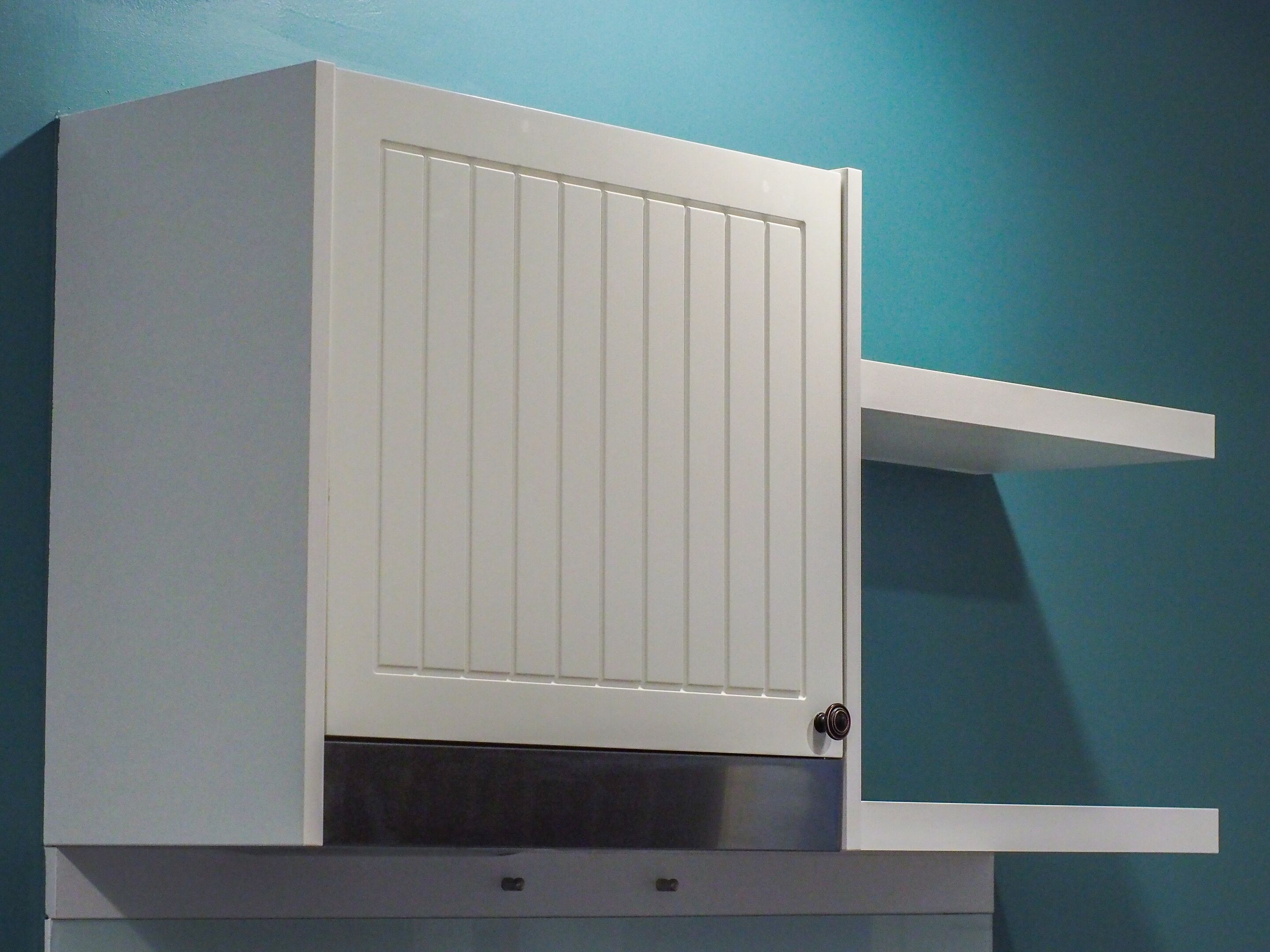A white cabinet with a door, a shelf, and a handle.