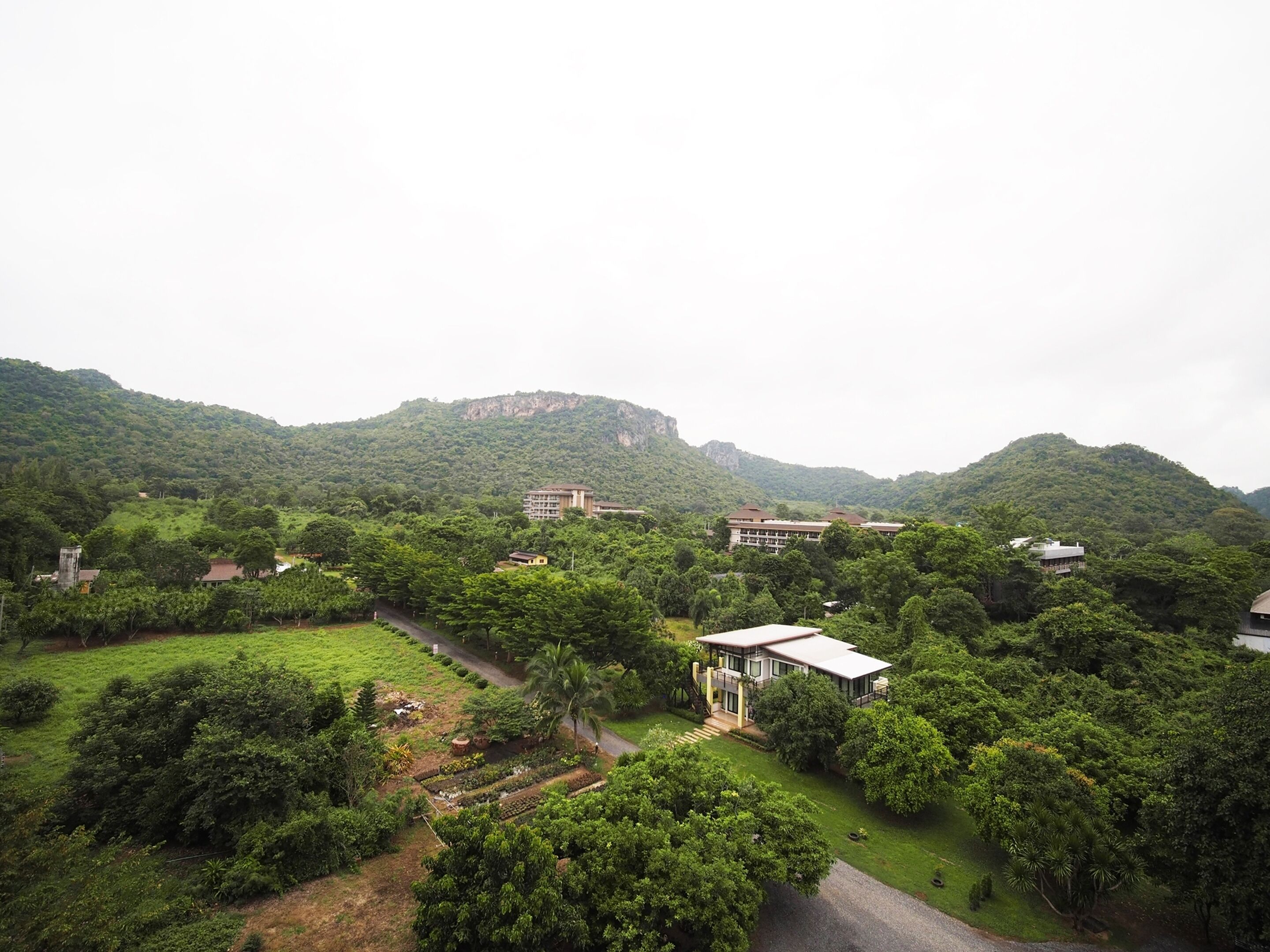 A residential area with a large building surrounded by lush greenery and hills in the background.
