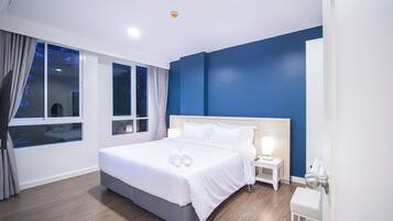 A modern hotel room with a large bed, bedside tables, a nightstand, a small desk, and a window with curtains.