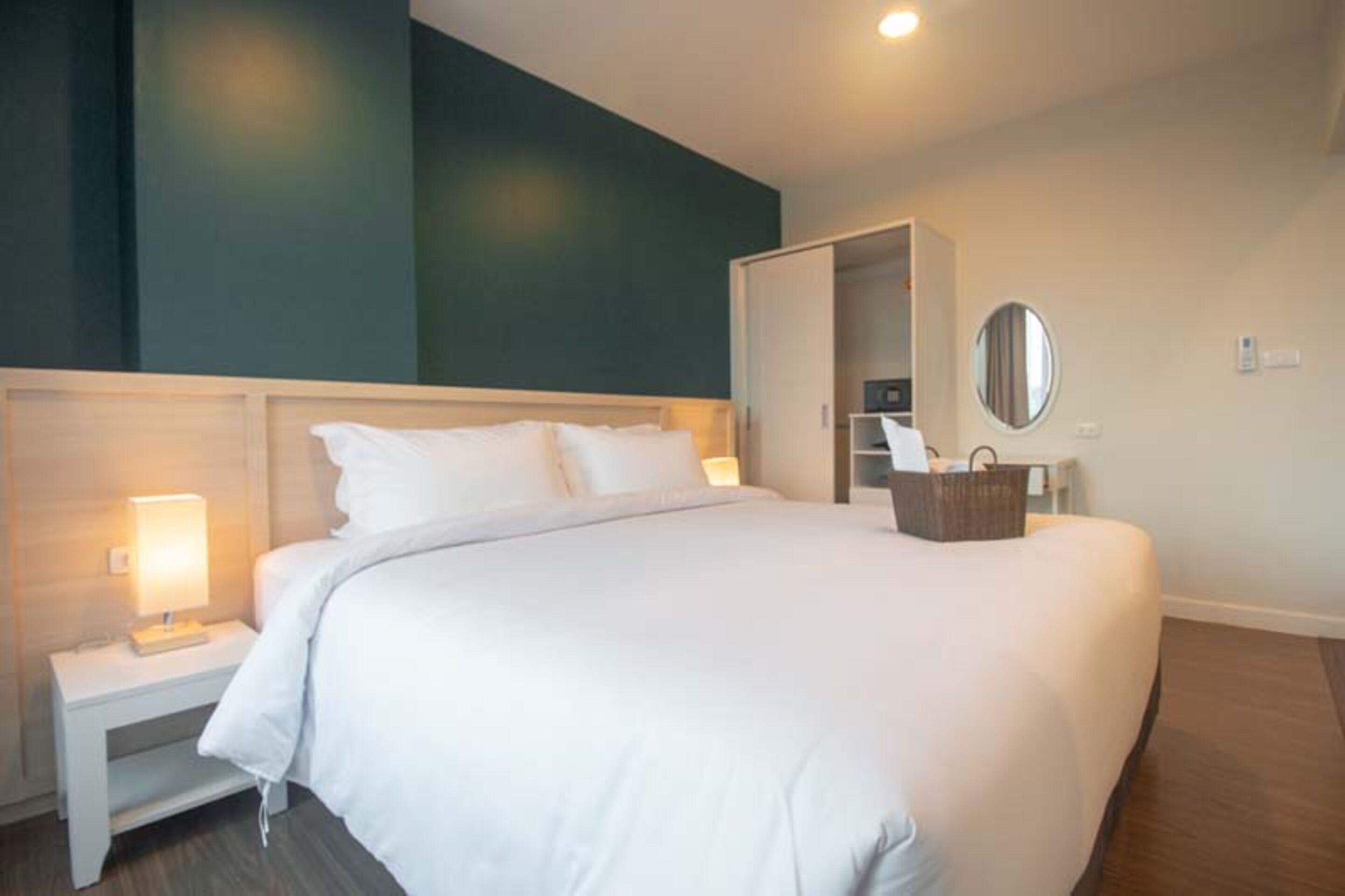 A modern hotel room with a large bed, bedside tables, a wardrobe, and a mirror.