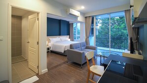 A modern hotel room with a bed, a sofa, a desk, and a balcony with a view of greenery. - Fortune Courtyard Khao Yai Hotel Official (Pak Chong)