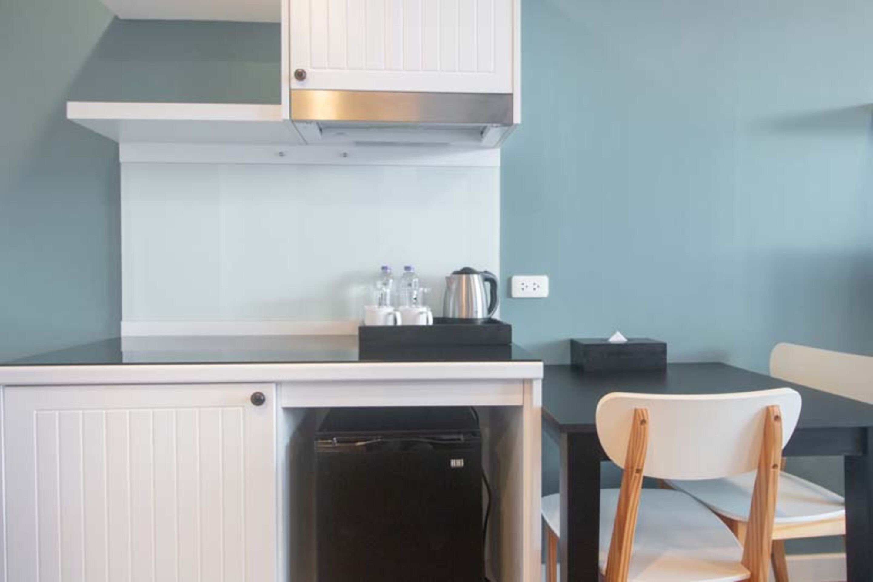 A compact kitchenette with a built-in stove, a small refrigerator, and a dining area with a chair and table.