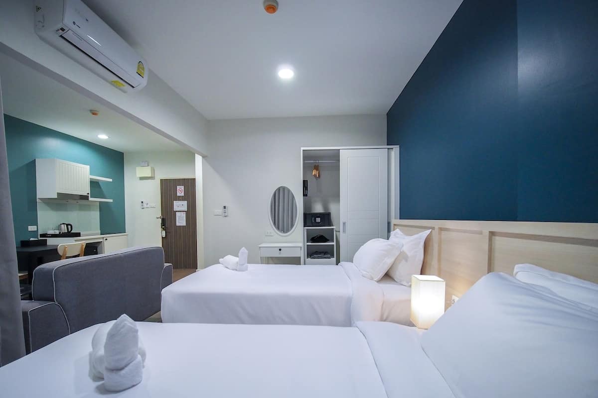 Ett hotellrum med två sängar, ett skrivbord, en stol, en garderob och ett litet kök.