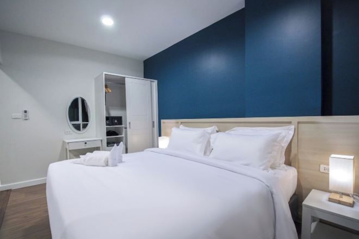 Ein modernes Hotelzimmer mit einem großen Bett, einem Kleiderschrank, einem Nachttisch mit Lampe und einem Spiegel an der Wand.