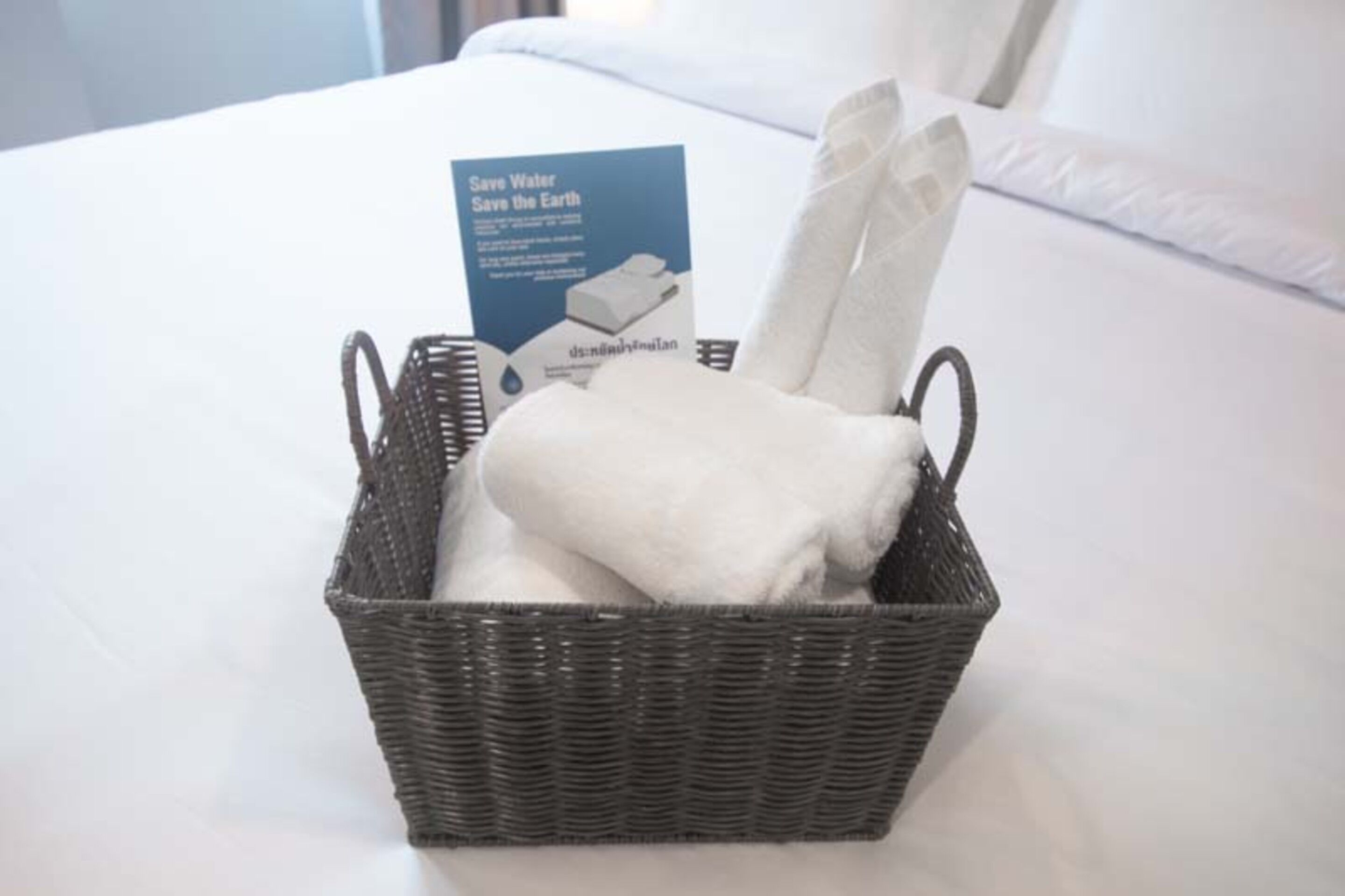 A wicker basket with a folded towel and a water-saving brochure on a bed.
