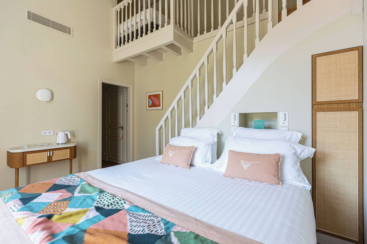 Habitación de hotel con cama, escritorio, silla, ventana y una escalera.