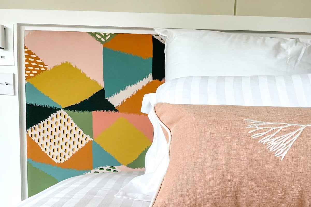 Una cama con colchón a rayas, una almohada blanca y una almohada color melocotón con diseño de hoja.