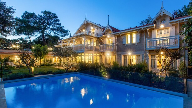 Un grand bâtiment à deux étages, avec une piscine devant.