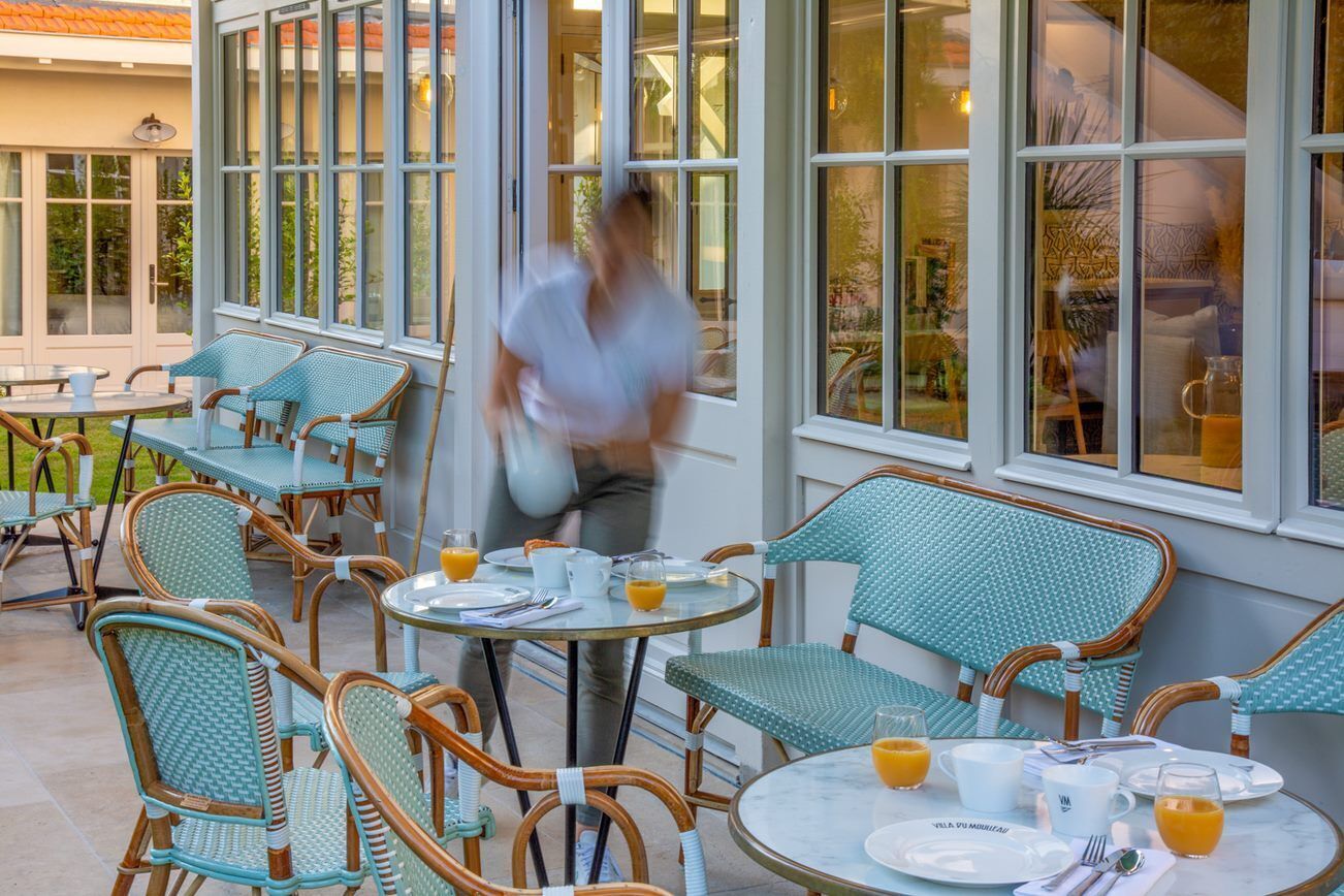 Un área de estar al aire libre con sillas y mesas de mimbre, algunas con alimentos para el desayuno.