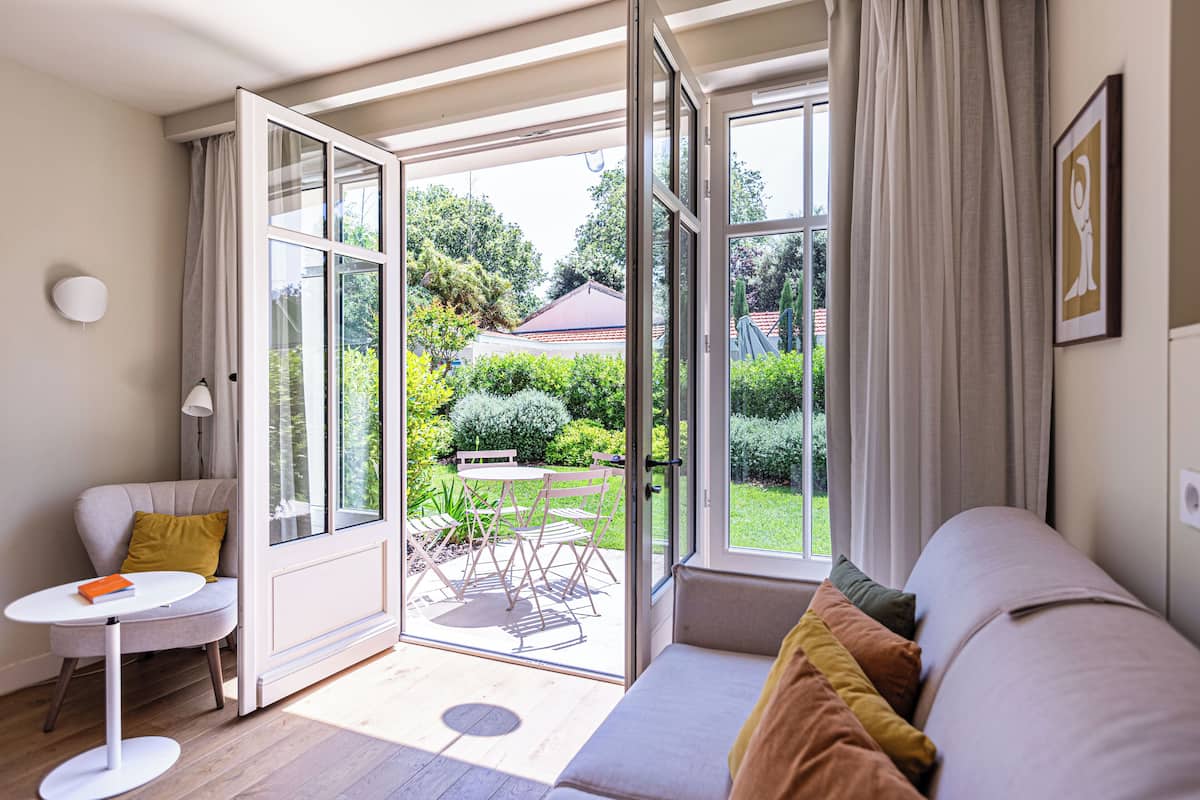 Una sala de estar moderna con un sofá, una mesita y un ventanal corredizo que da a un jardín.
