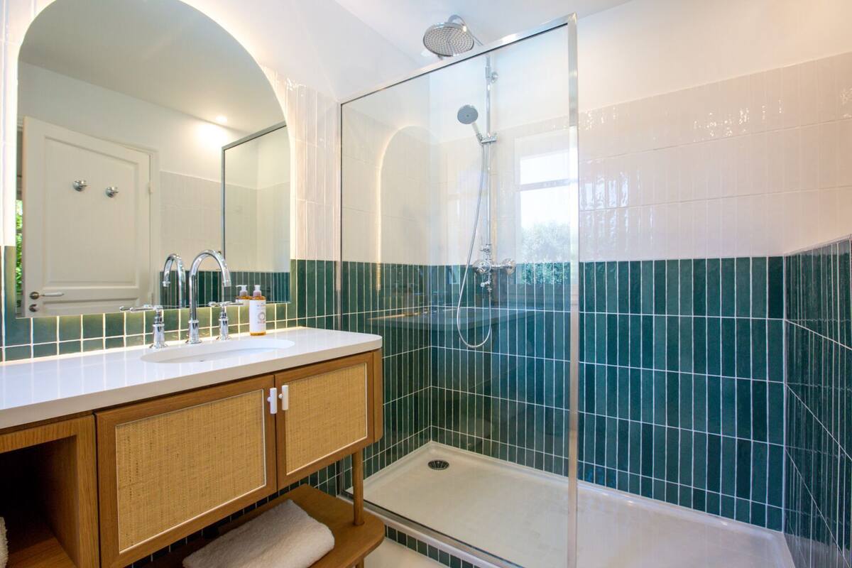 Un baño con ducha de vidrio, un lavamanos con espejo y pared de azulejos.