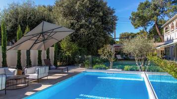 A swimming pool with lounge chairs and an umbrella, surrounded by trees and a building.