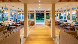Un vaste espace de salle à manger avec de hauts plafonds, de grandes fenêtres et un espace central ouvert donnant sur un jardin.