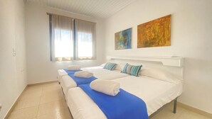 Une chambre d’hôtel avec deux lits, une grande fenêtre avec des rideaux et deux tableaux abstraits accrochés au mur.