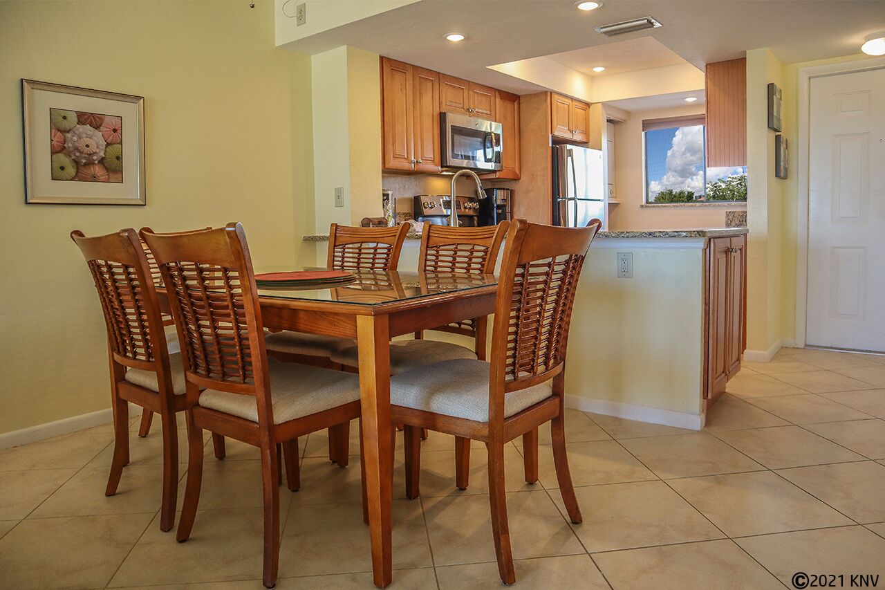 A dining area with a wooden table and chairs, a kitchen with wooden cabinets and appliances, and a window with a view of the sky.