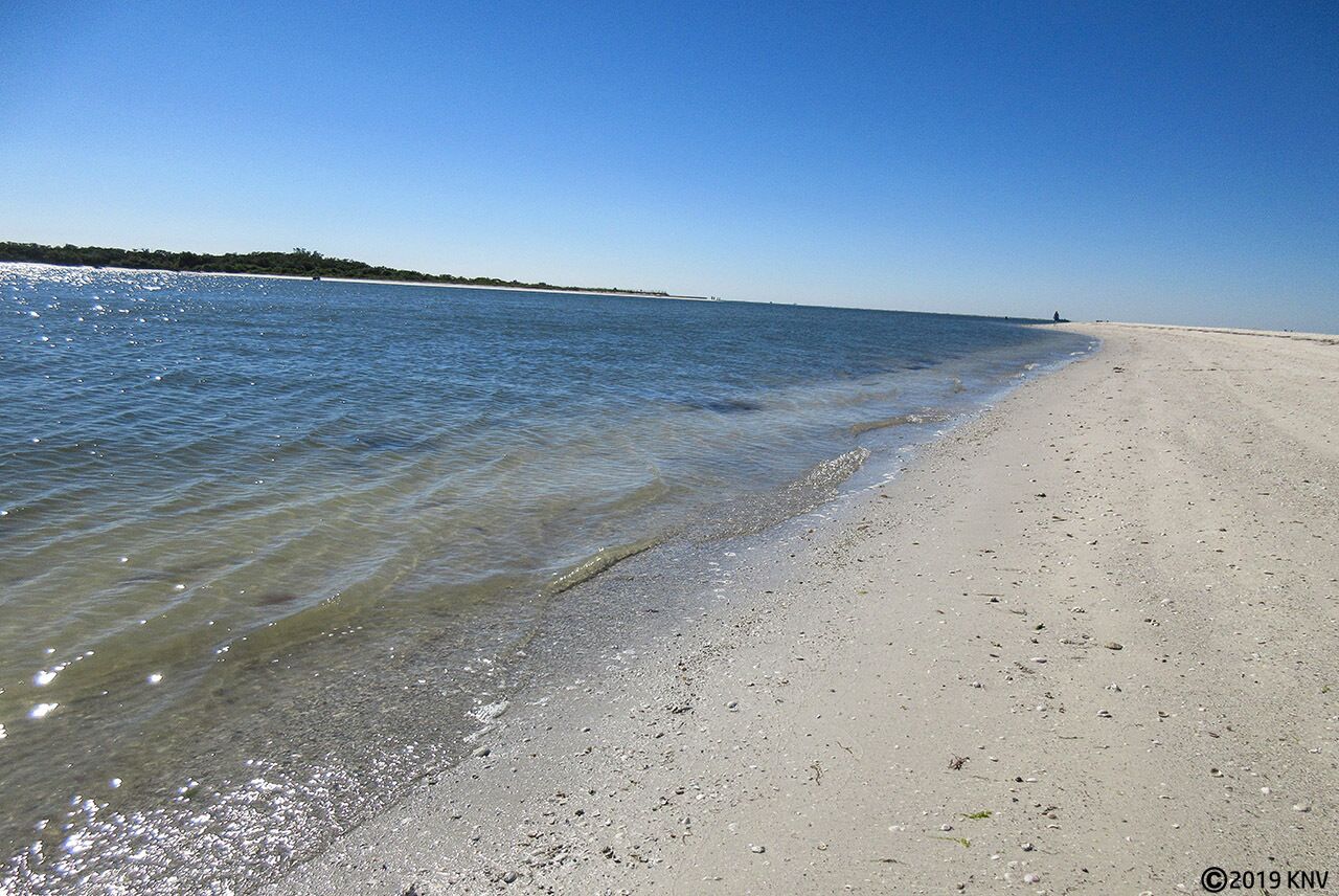 Une plage à l’eau claire, avec un rivage sablonneux et un horizon lointain.