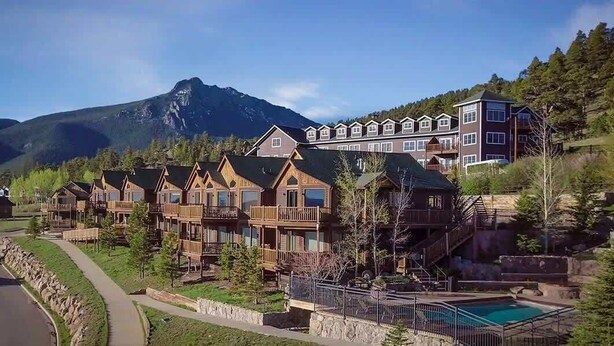 Un complexe hôtelier comprenant plusieurs chalets en bois et un grand bâtiment doté de balcons, le tout situé dans un cadre montagneux.