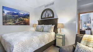 Une chambre à coucher comprenant un lit, des tables de chevet, une chaise, un élément décoratif mural et un tableau représentant un paysage de montagne.