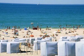 A beach with striped beach umbrellas and lounge chairs, a sandy shore, and the ocean in the background.