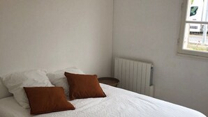 Siististi pedattu sänky, jossa on valkoiset ja ruskeat vuodevaatteet, huoneessa, jonka seinät ovat valkoiset ja jossa on ikkuna.